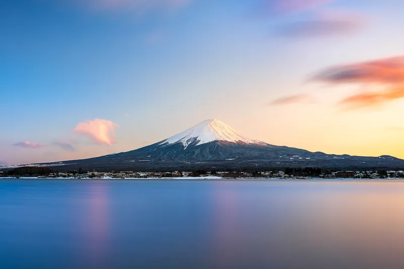 Mount Fuji with a snow-capped peak above a calm lake at sunset