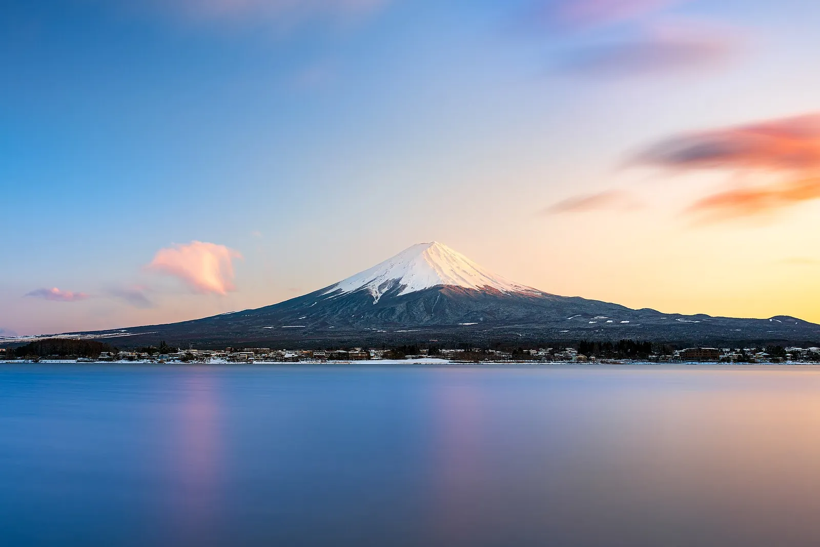 Mount Fuji with a snow-capped peak above a calm lake at sunset