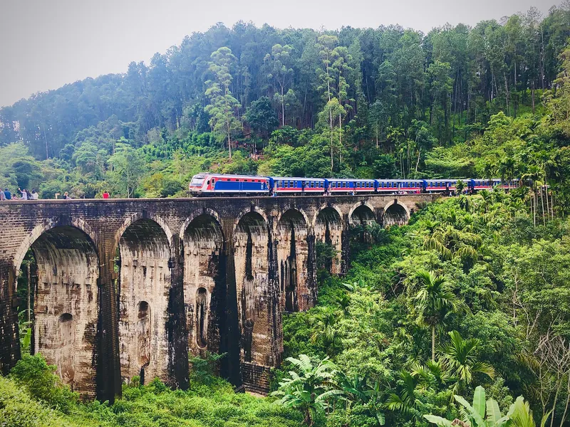 A train crossing the Nine Arch Bridge in Ella, Sri Lanka, surrounded by green forest